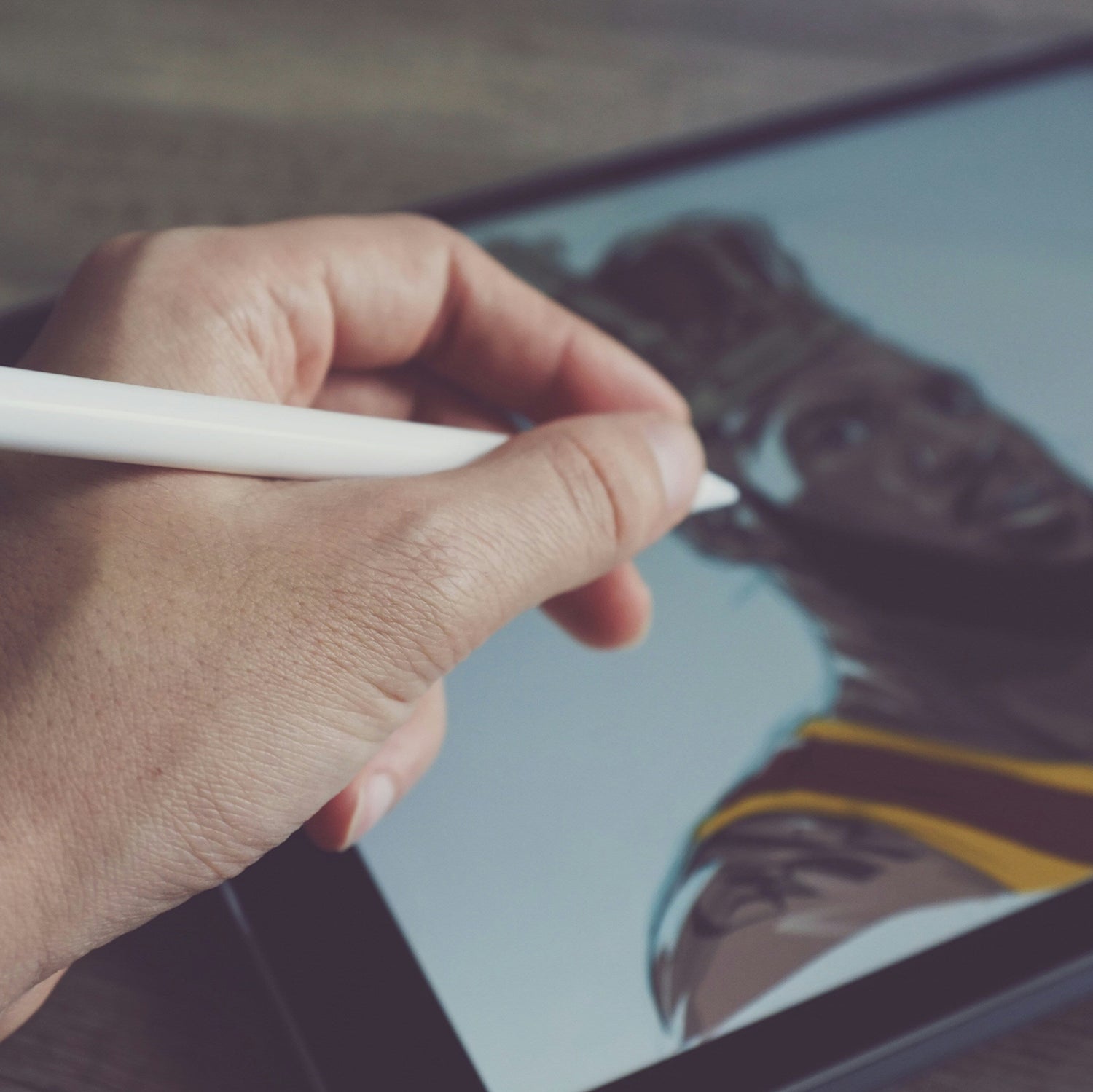 Hand holding a stylus over a tablet displaying a photo of a person wearing a cap.